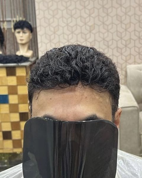 شعر داكن مموج وقصير لعميل بعد تركيب نظام الشعر وقصه، والوجه مغطى جزئيًا بمرآة